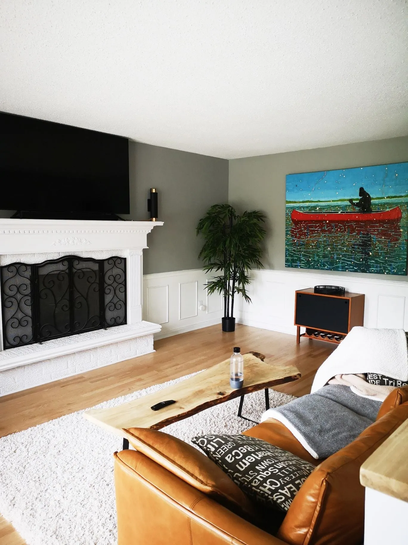 A finished basement family room with a white fireplace surround, a wall-mounted TV and a leather sofa