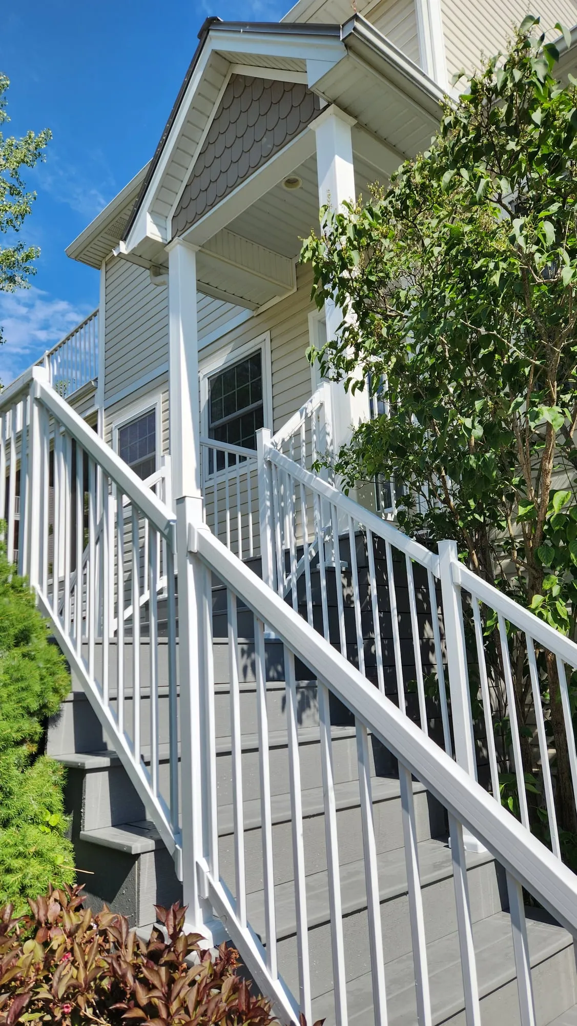 Grey stairs seen from below, white railings climbing to a covered porch with a scalloped-shingle gable.