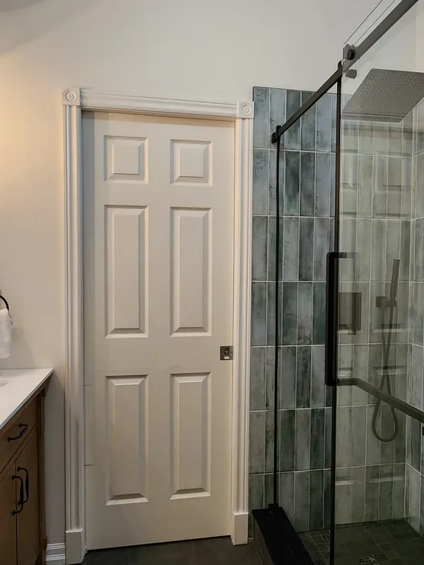 A finished bathroom with a wood-toned vanity, black-framed mirror and a glass shower lined in grey-green tile.