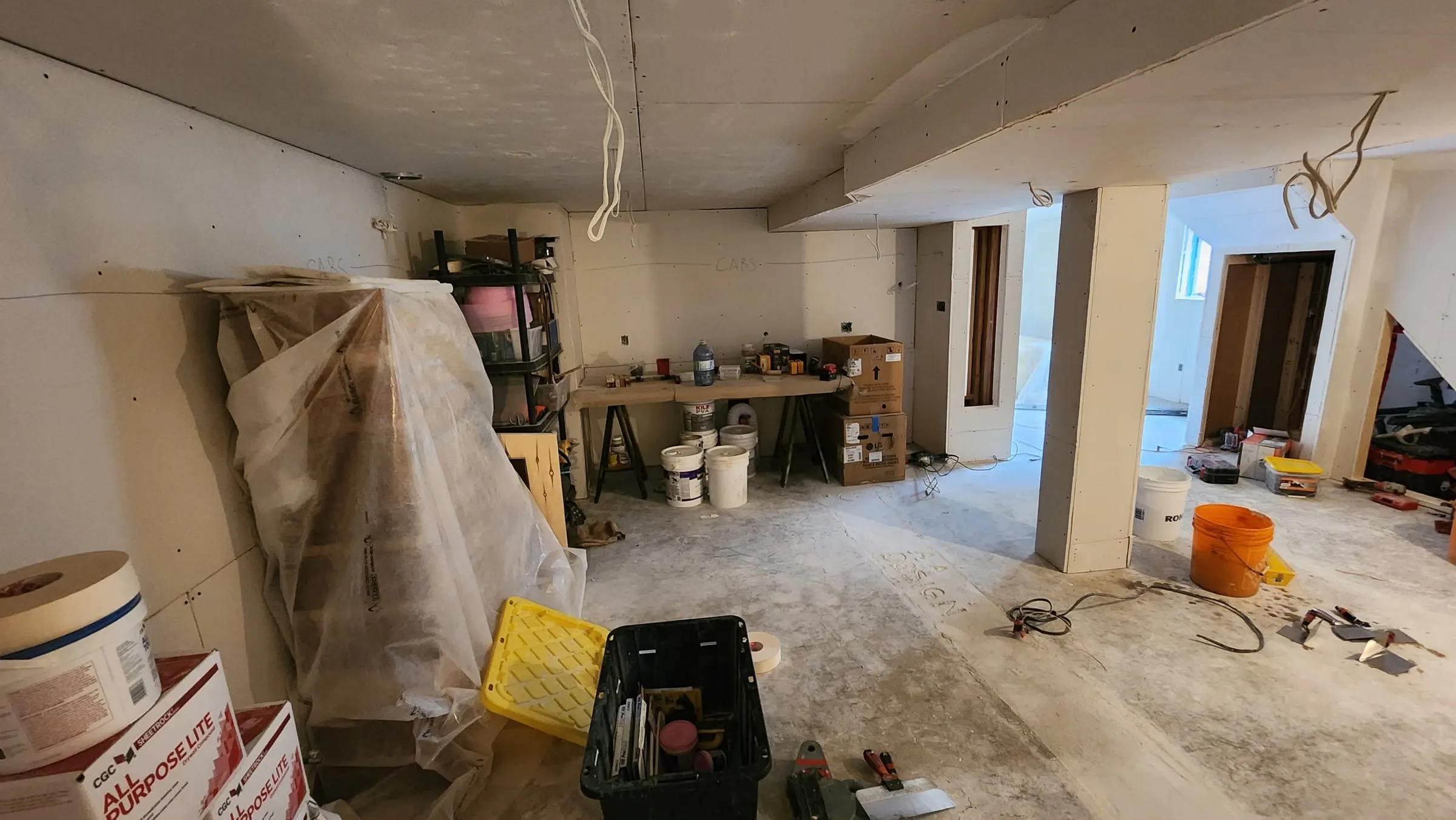 The basement with new drywall up, the posts boxed in and tools spread across the concrete floor.