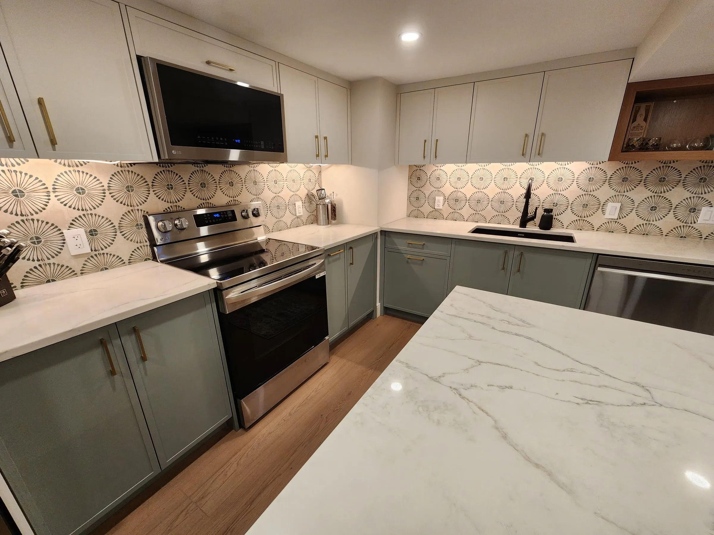 The range with a microwave above it among white upper cabinets, a patterned tile backsplash, and the island's veined top in front.