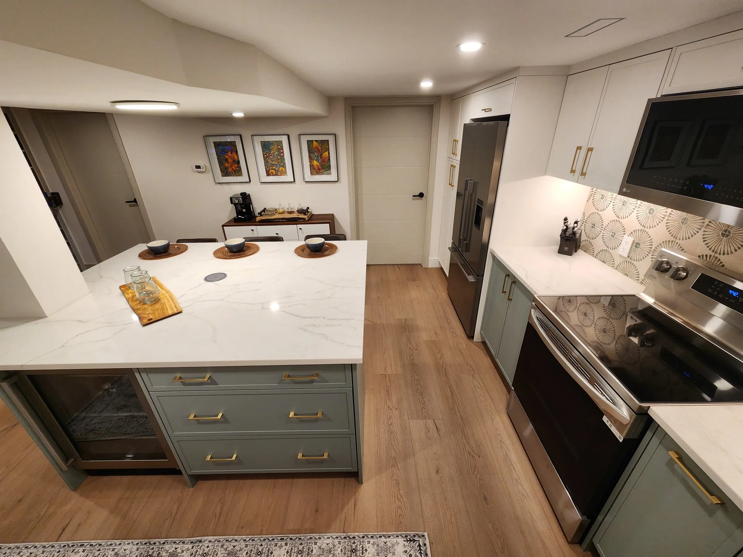 The kitchen from the end of the island, with a beverage fridge in the island and framed prints on the far wall.