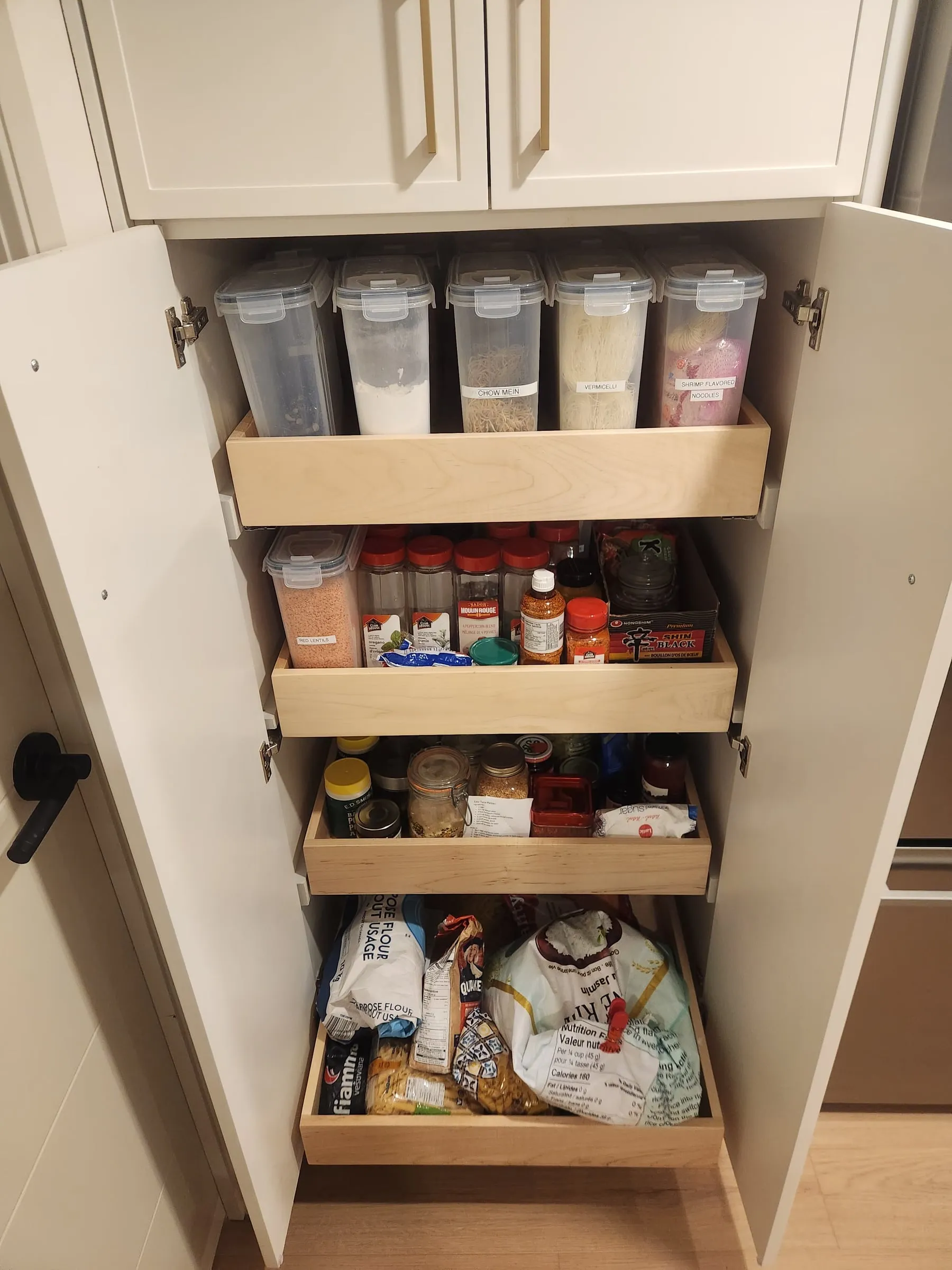 A pantry cabinet open to show four pull-out drawers with storage containers and food.