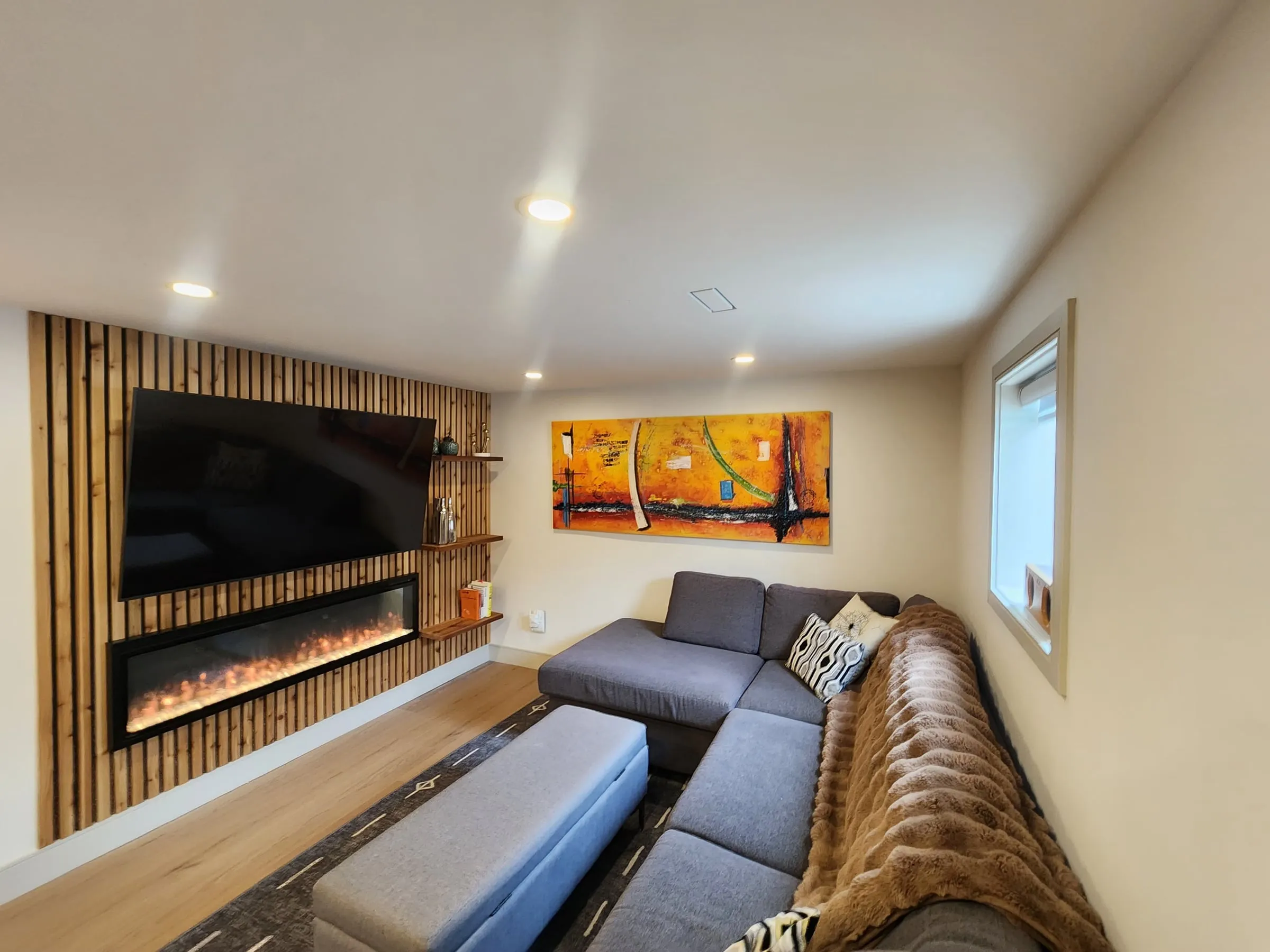 A living room with a wood slat feature wall, a wall-mounted TV above a long linear fireplace, and a grey sectional sofa.