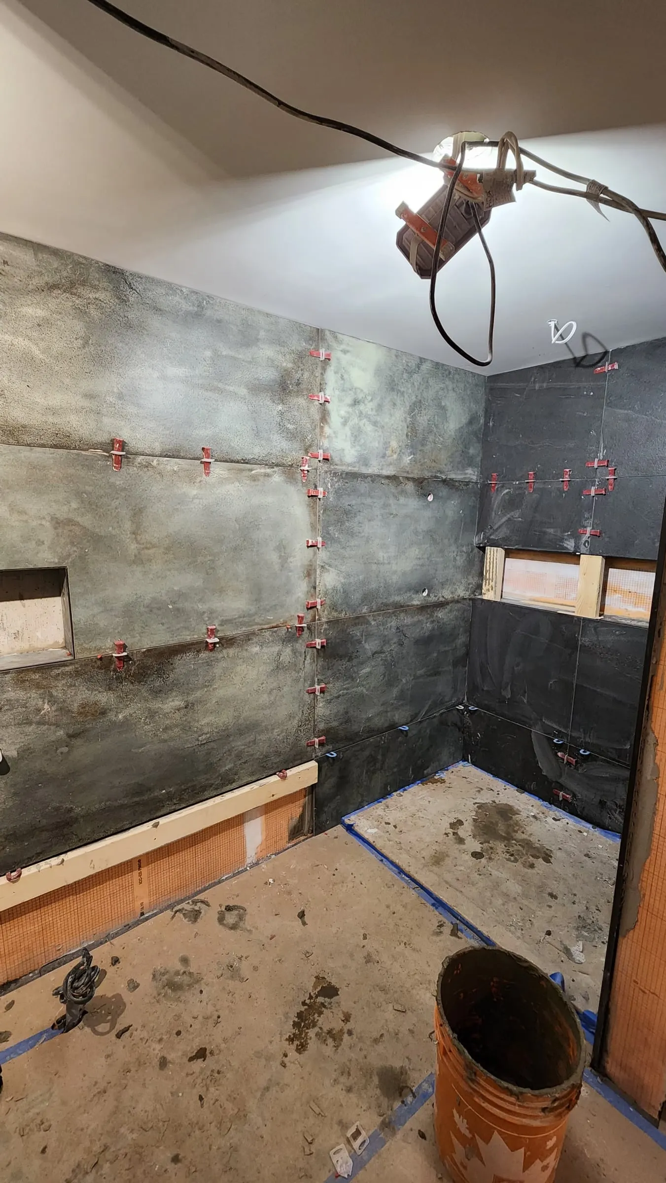 Large dark grey-green tiles going up the walls with red levelling clips, around a long niche.