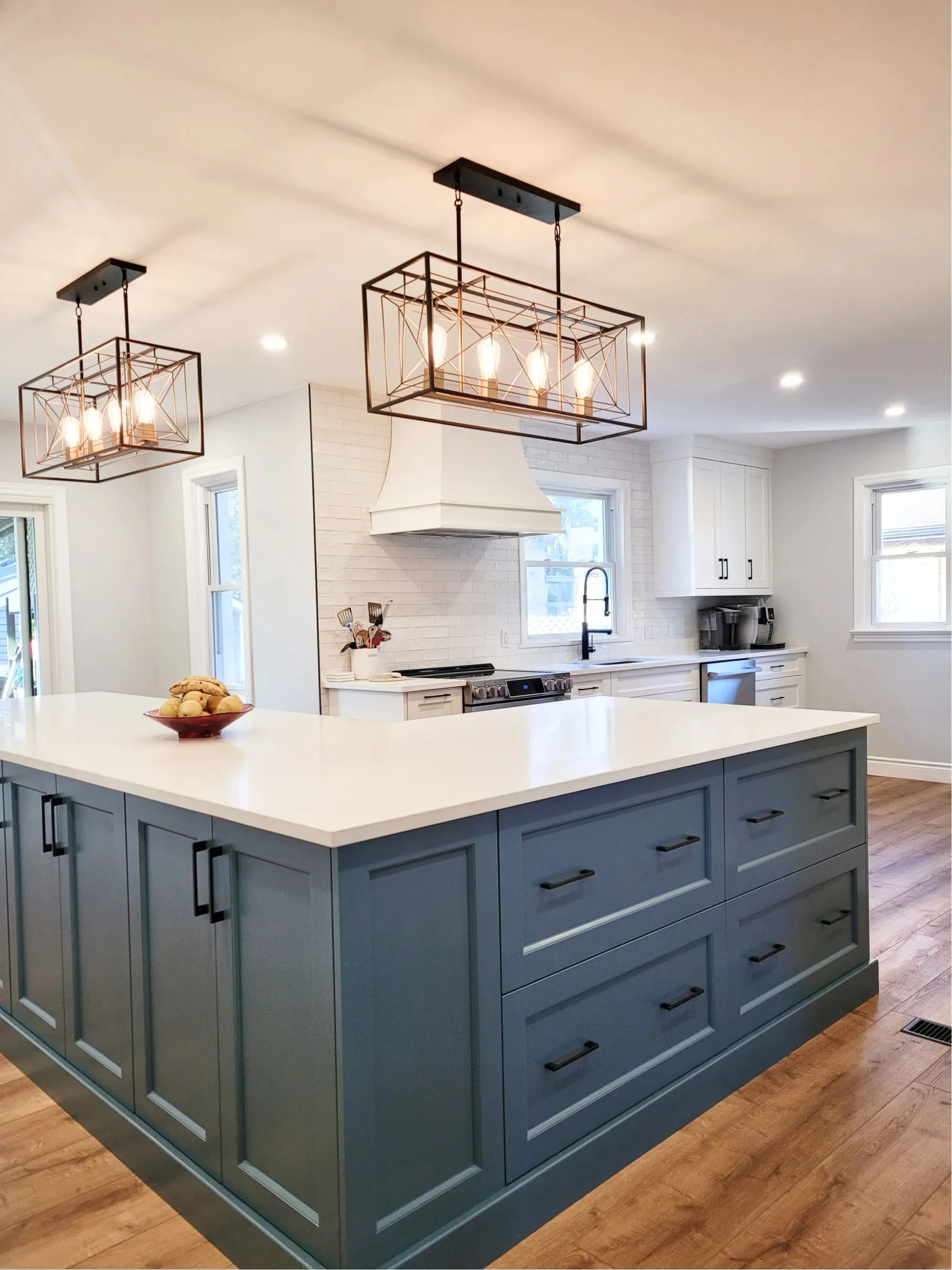 A renovated kitchen with a blue island, a white countertop and two black cage pendant lights