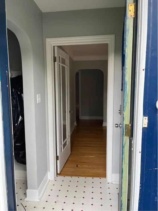 The front entrance before the work, with a worn blue door, patterned floor tiles and a grey hallway.
