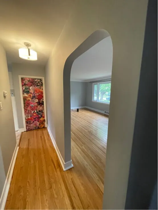 The main floor before: a grey hallway beside an arched opening into a bright room with wood floors.