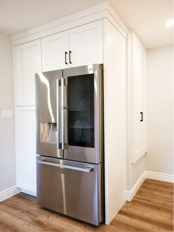 The finished kitchen's silver French-door fridge, built into tall white cabinets with black handles.