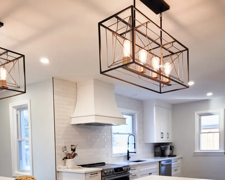 Two black wire-frame pendant lights with exposed bulbs hang over the island, with the white range hood beyond.