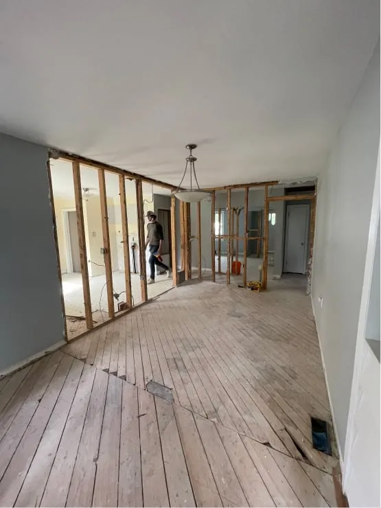 The dividing wall stripped to its wood studs during demolition, with the old floorboards exposed.