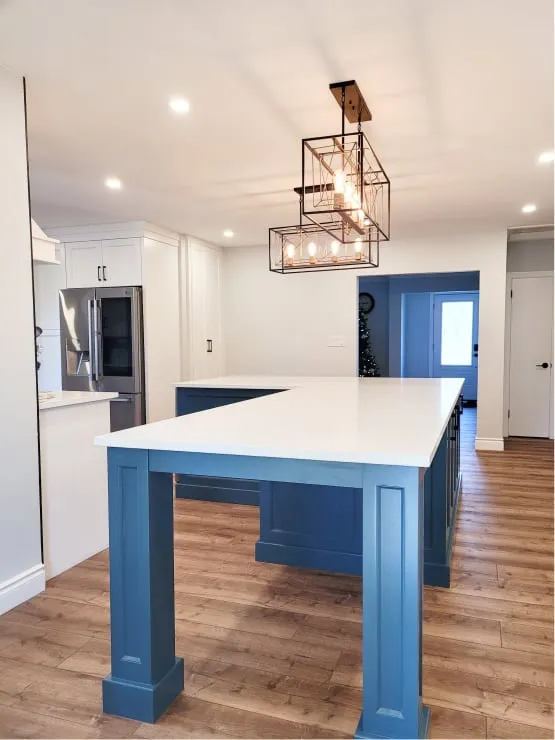 The finished open space with a large L-shaped blue island, white countertop and two black wire pendants above.