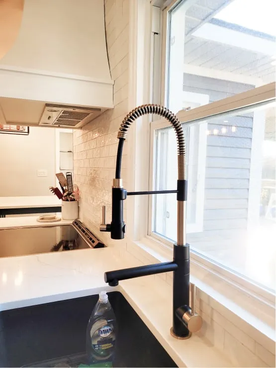 A black pull-down faucet with a coiled spring neck over a black sink, beside a large window.