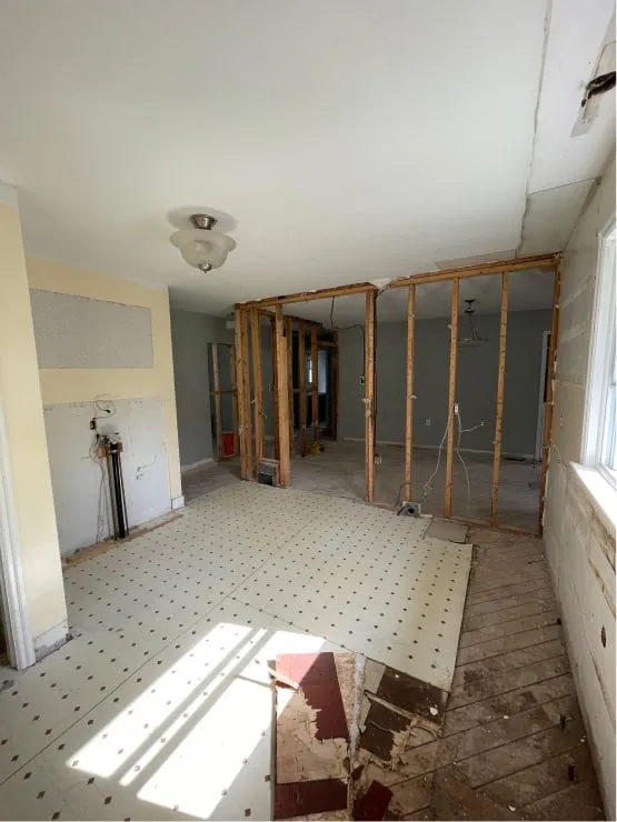 A yellow-walled room during demolition, with one wall open to bare studs and the old flooring torn up.