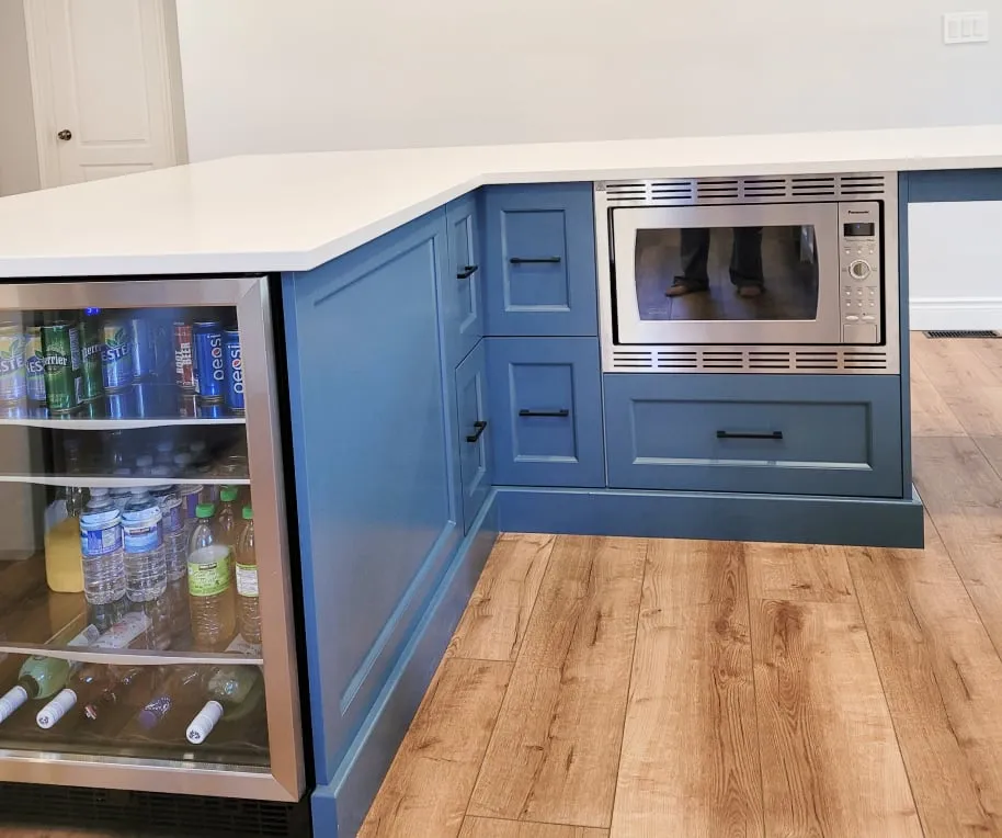 The blue island's corner, with a glass-door beverage cooler full of drinks, a microwave and black-handled drawers.