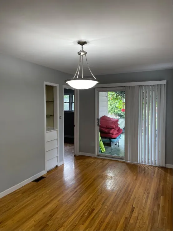 The dining room before: grey walls, a bowl pendant light, wood floor and a patio door with blinds.