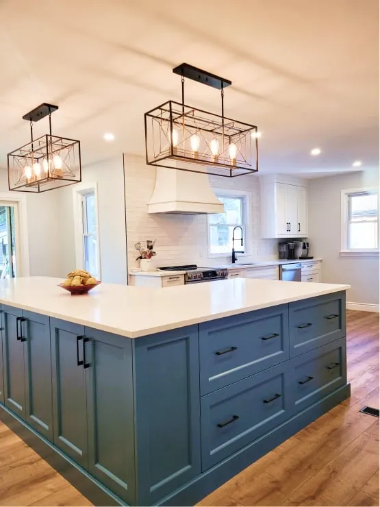 The open dining and kitchen area after, with a long blue island under two black wire pendant lights.