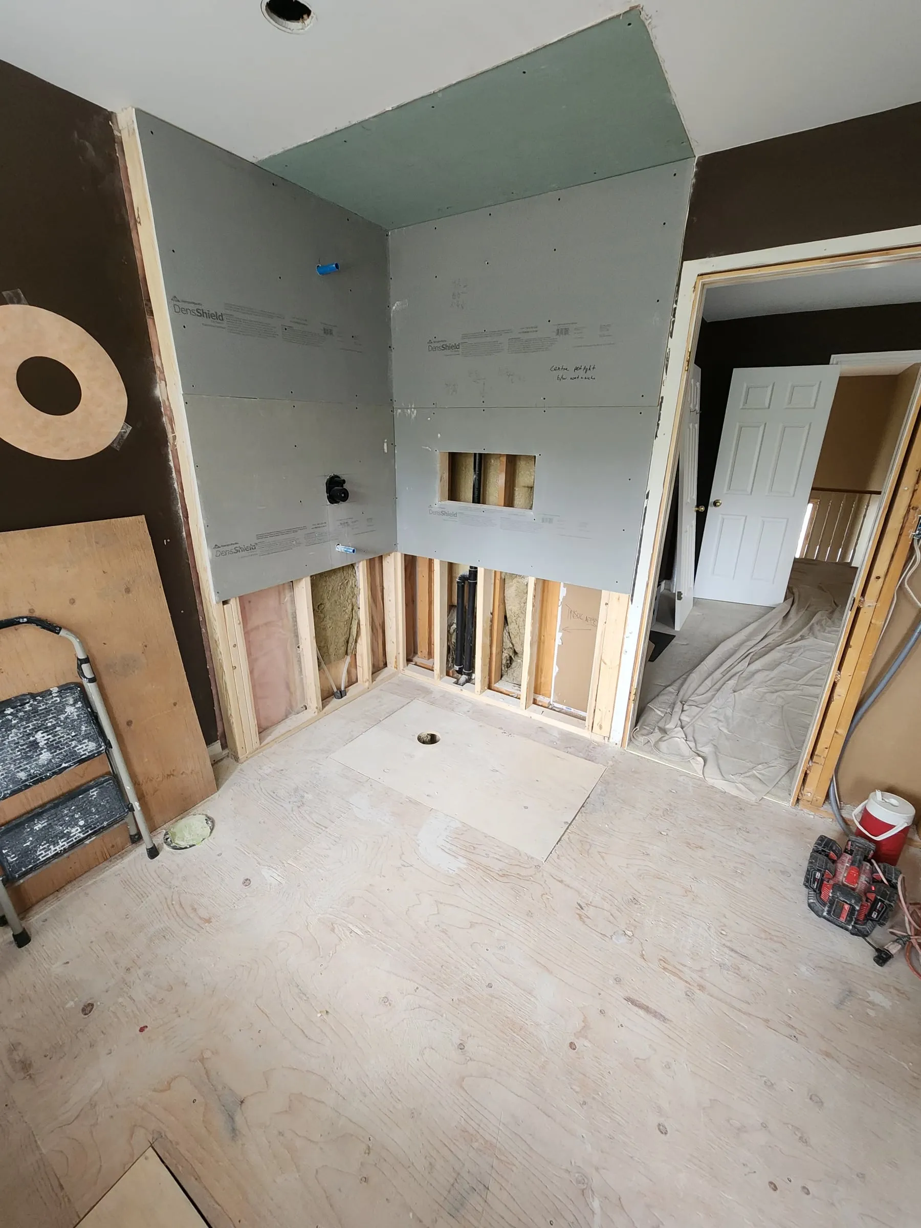 New backer board on the upper shower walls, with an opening for the plumbing, the studs still open below and the floor stripped to the subfloor.