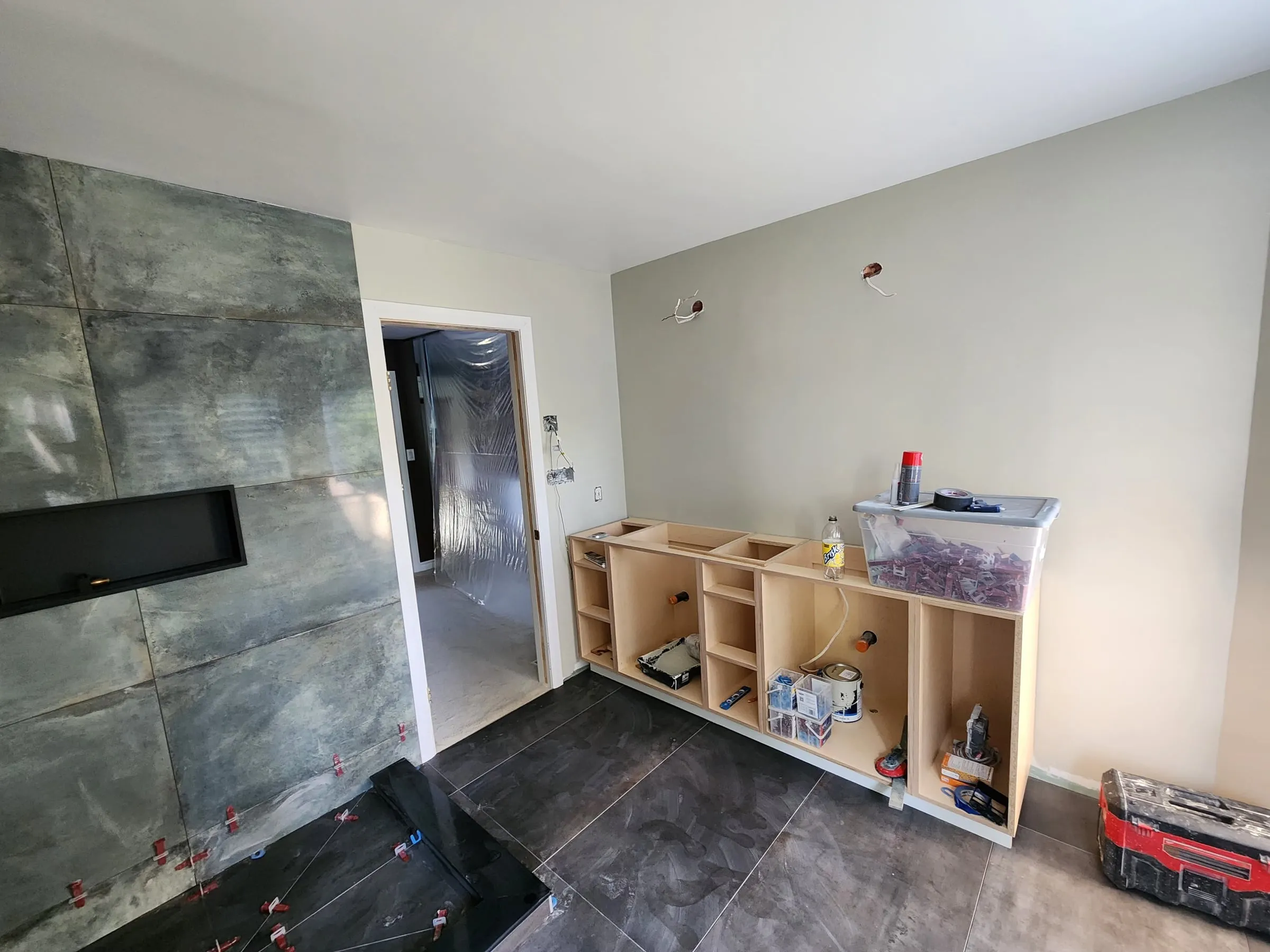 The new tiled shower wall with a long niche, the dark tile floor down, and the vanity cabinet boxes set in place without doors or a top.