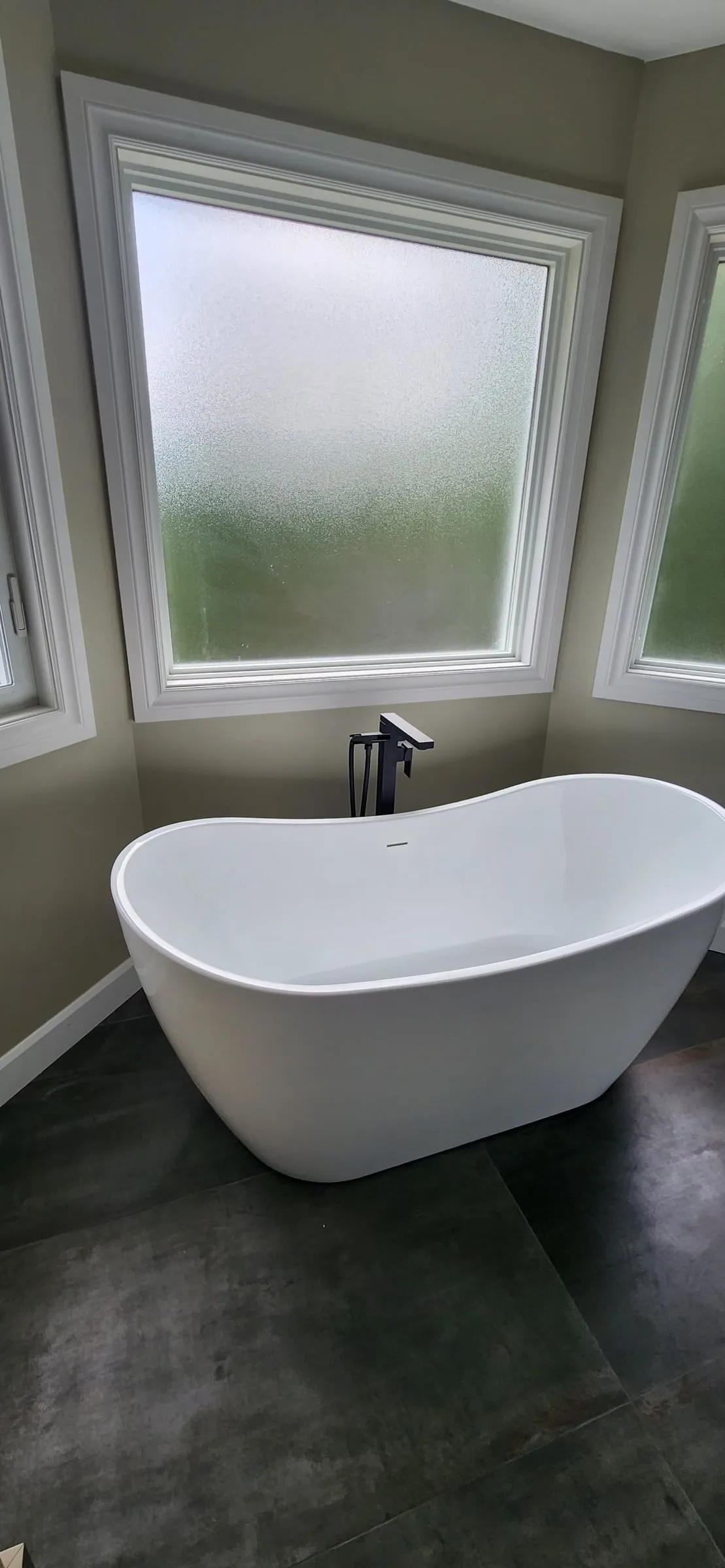 A white freestanding tub with a black floor-mounted faucet, below a frosted window.