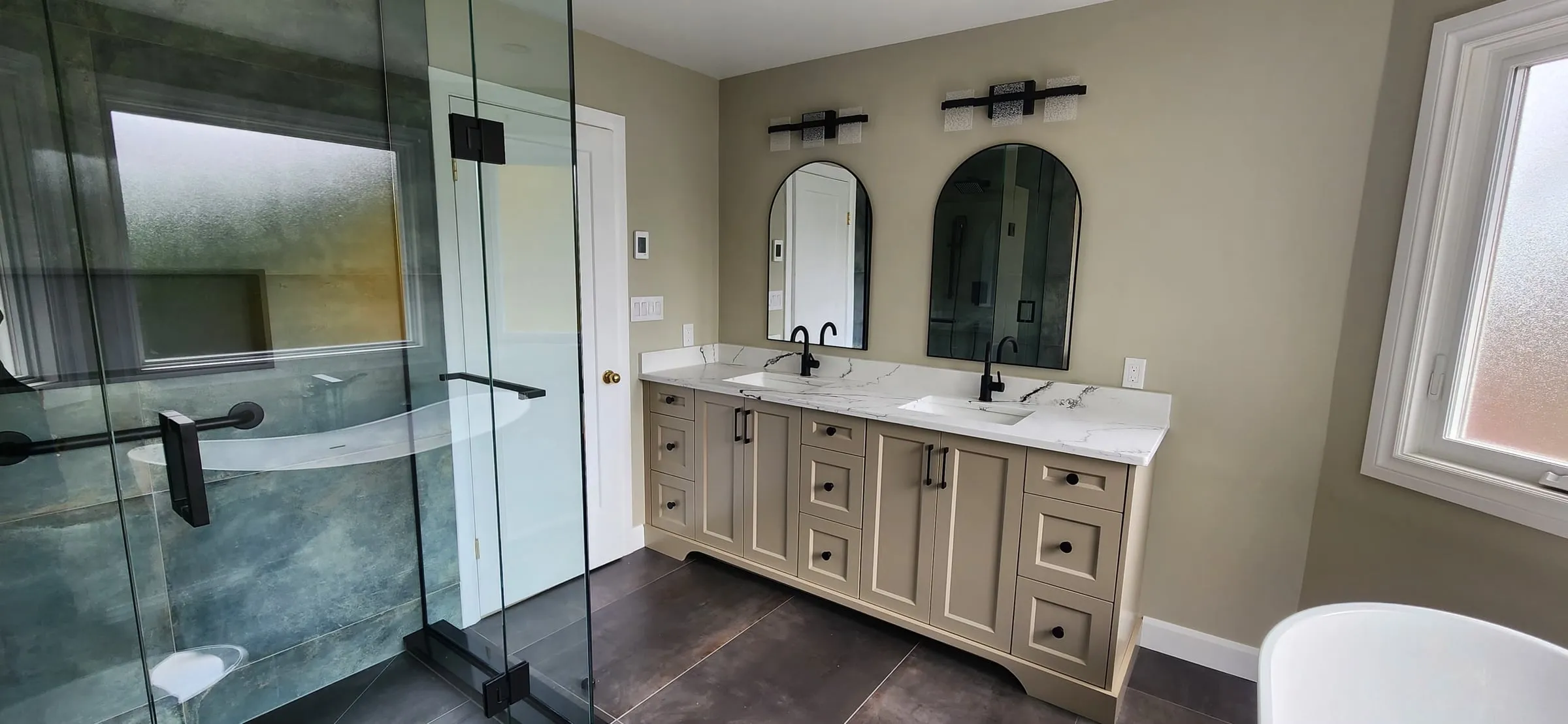 The glass shower and the double vanity side by side, with the arched mirrors and a frosted window on the right.