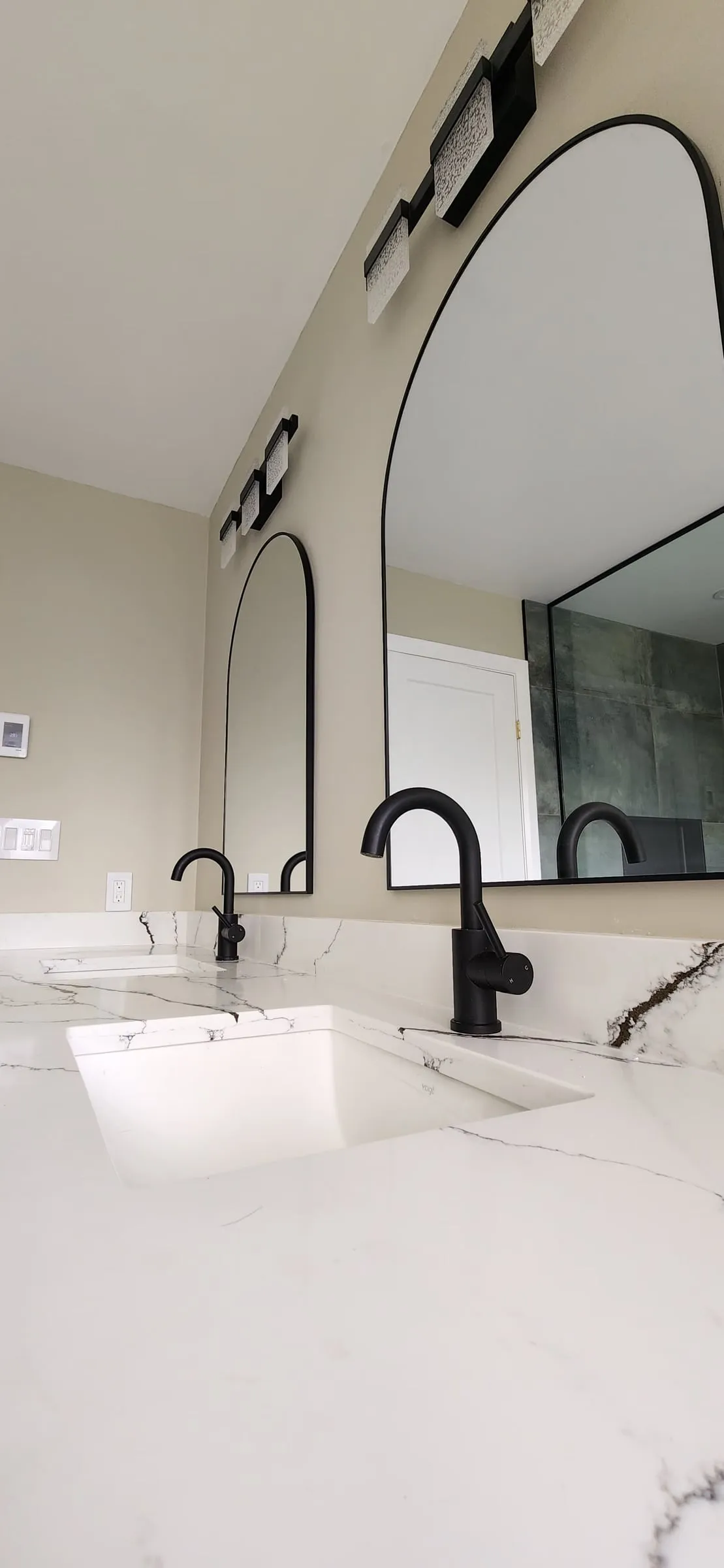 A white undermount sink and a black faucet on a veined counter, under the arched mirror.