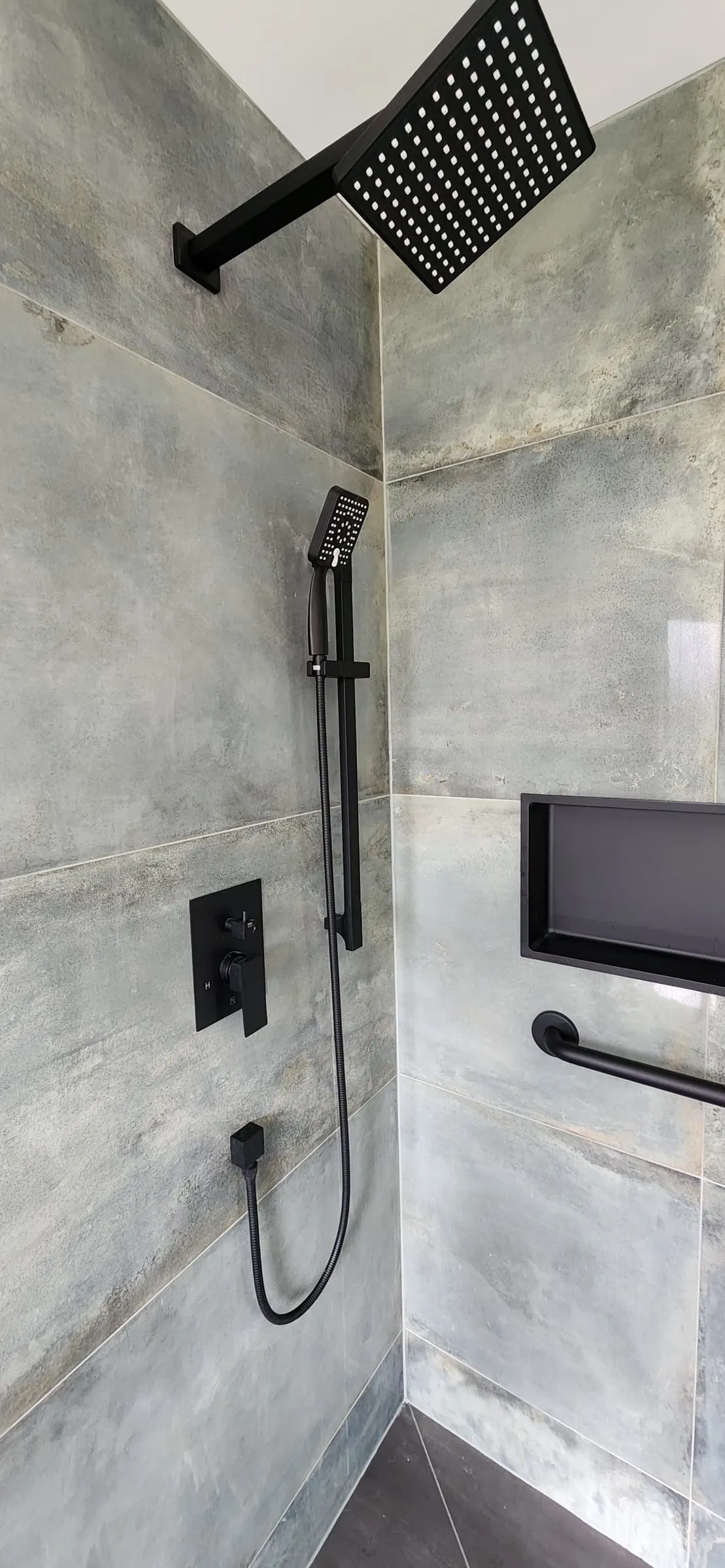 Inside the shower: a square rain head, a handheld spray on a slide bar, a recessed niche and a grab bar.