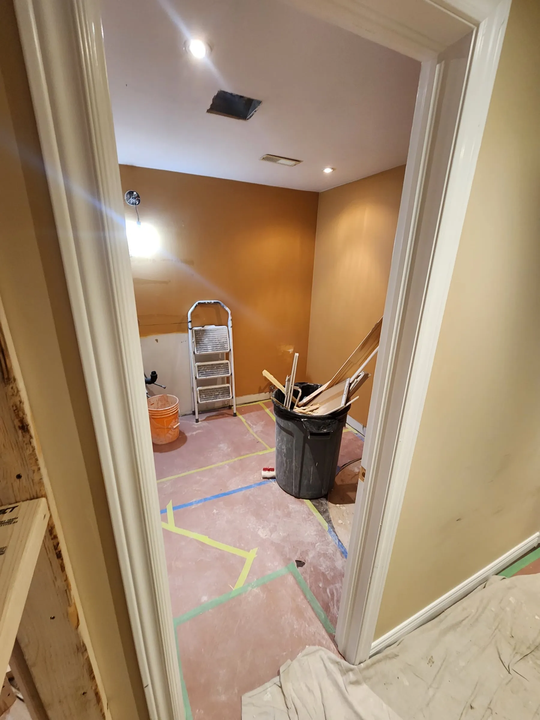 A basement room with orange walls, stripped out, with its floor covered and taped.