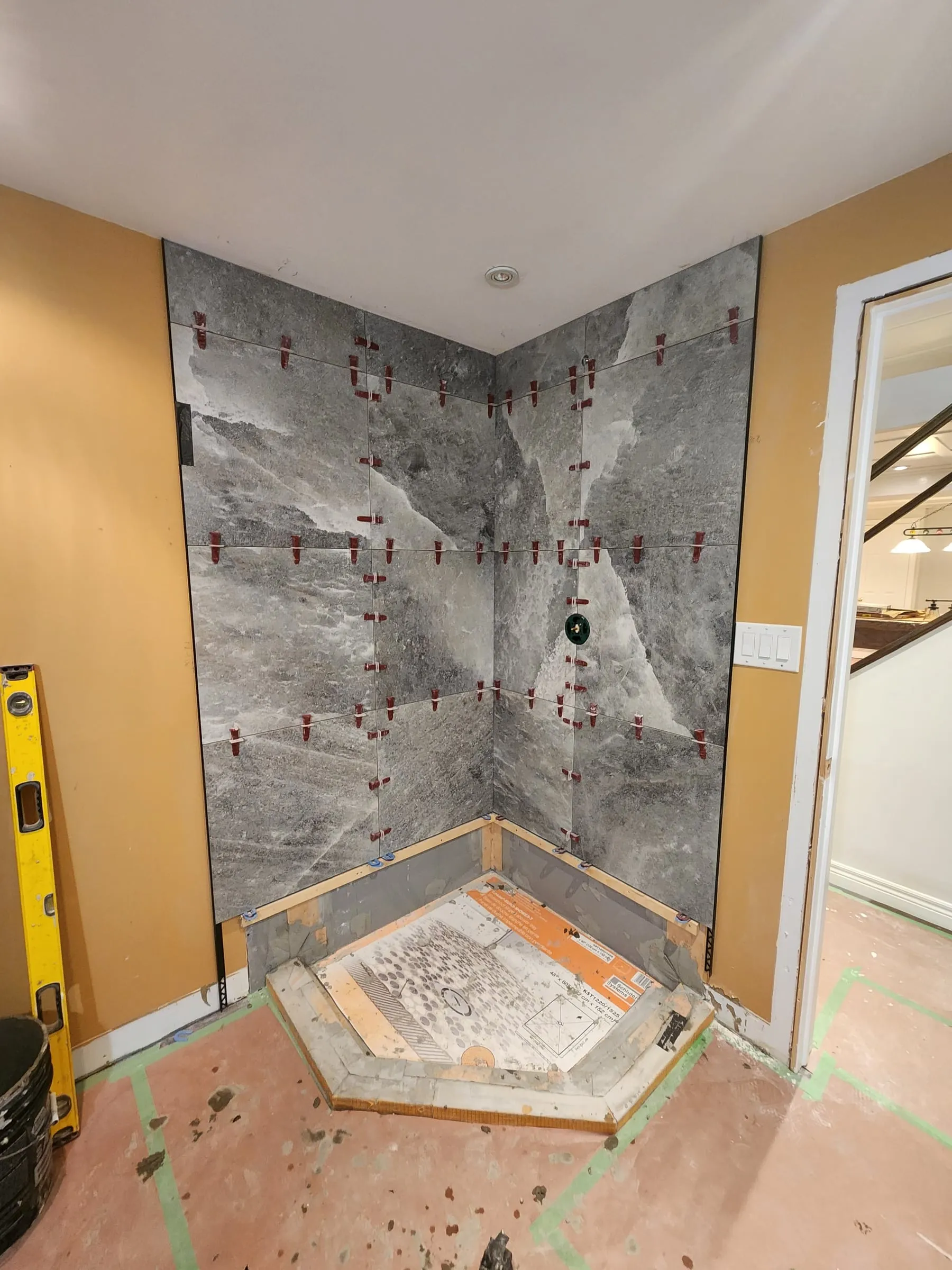 Grey stone-look tiles going up the corner shower walls, held with red levelling clips, above the new shower base.