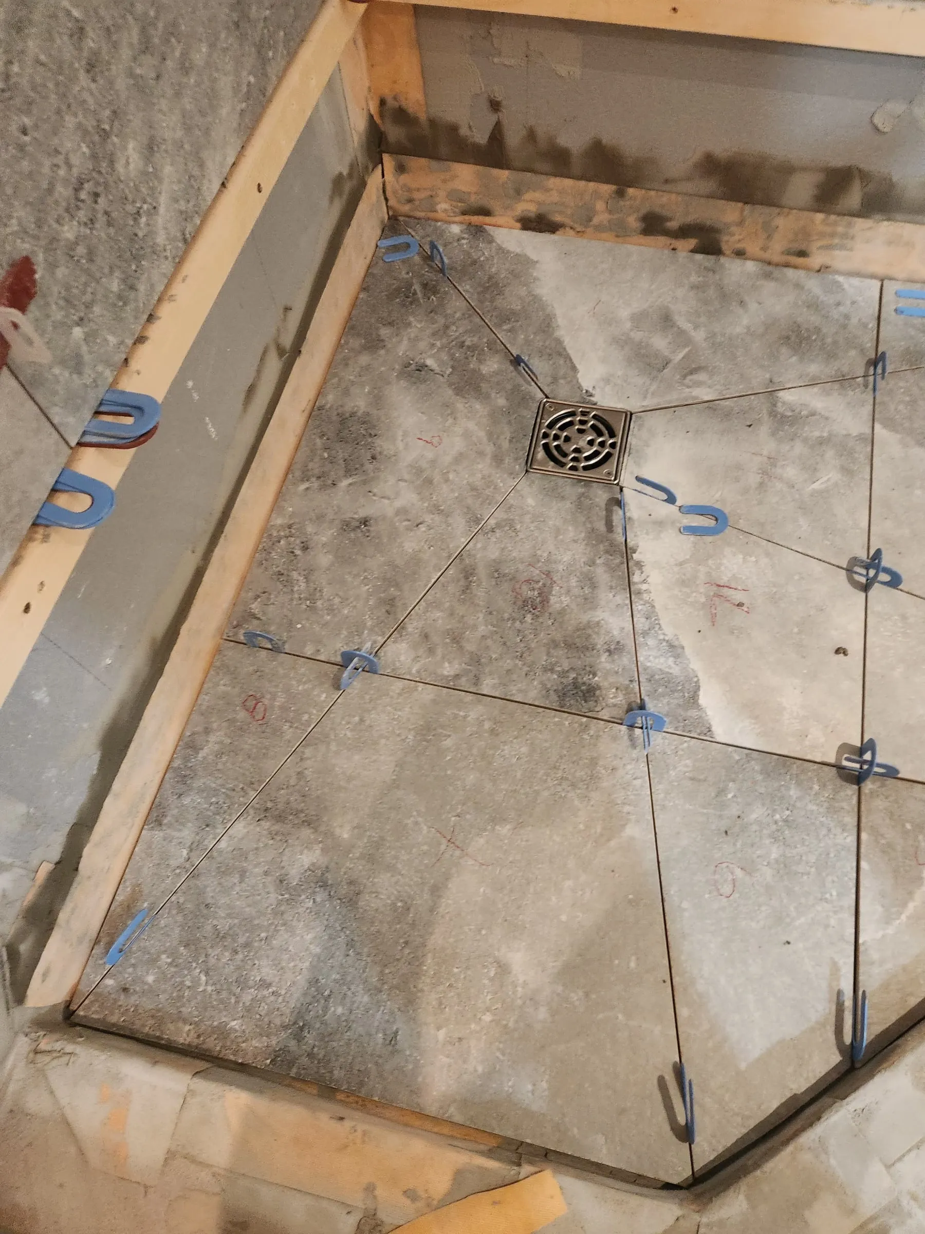 The shower floor tiled in large stone-look pieces around a square drain.