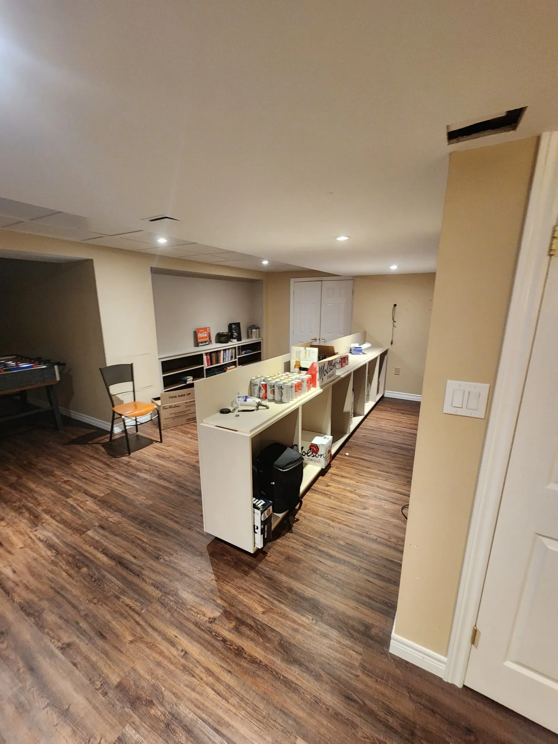 The basement before: a row of low white shelving units on a wood-look floor, with a foosball table on the left.