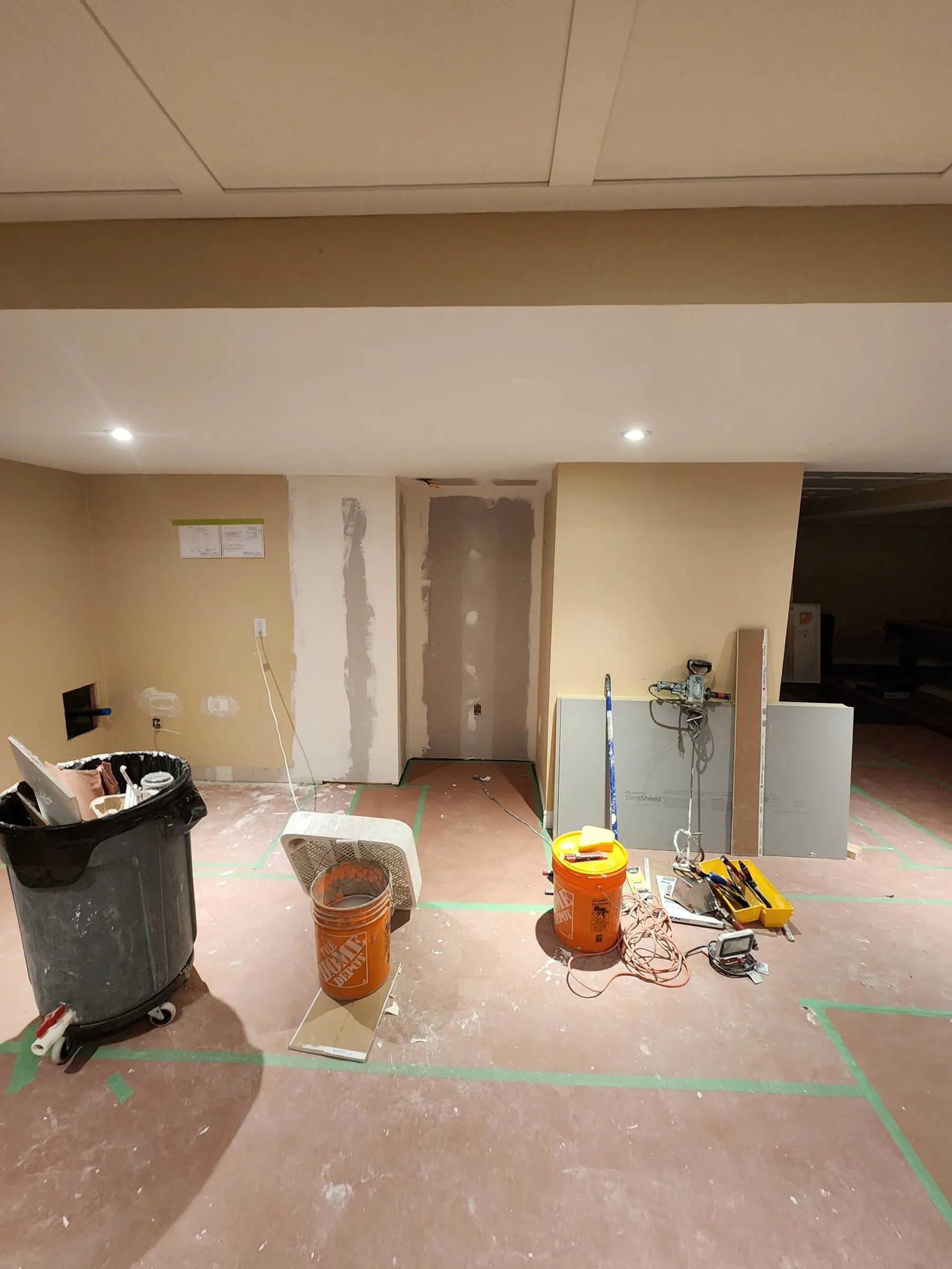 The bar area mid-work: the floor covered with protection board, fresh drywall patches on the end wall, and buckets and tools around the room.