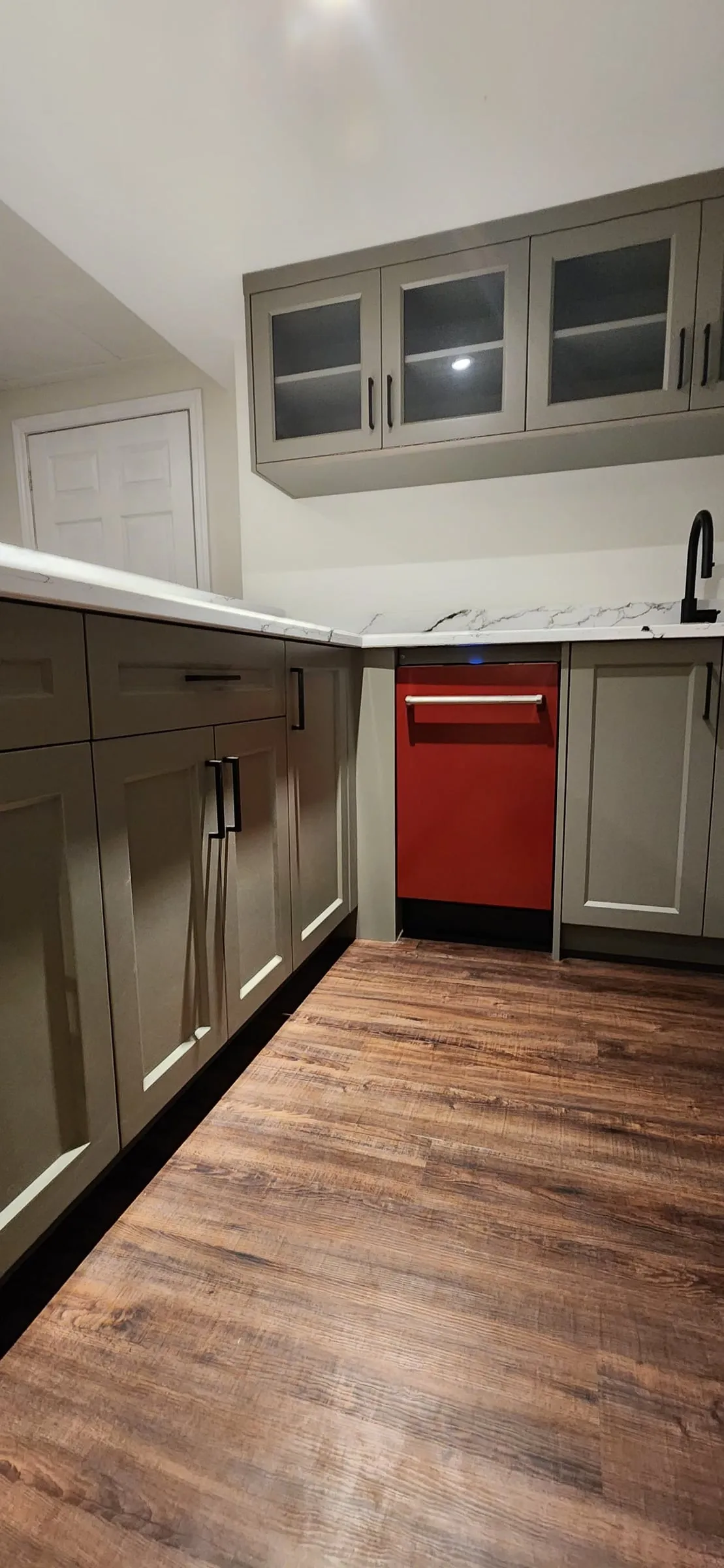 Sage-grey base cabinets, glass-front upper cabinets, a black faucet and a red dishwasher.