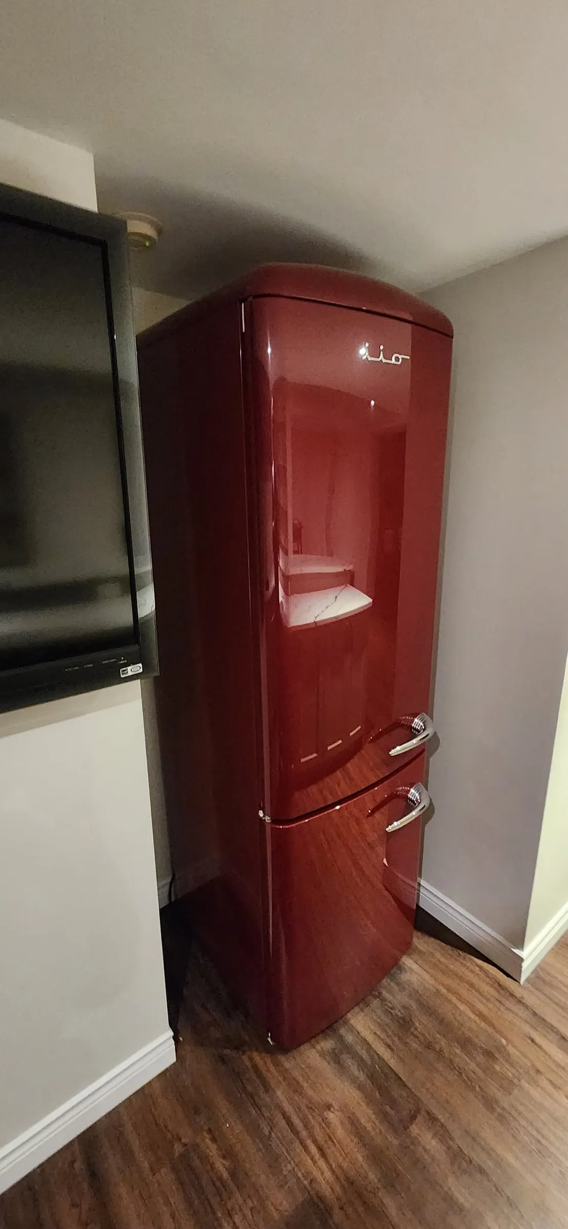 A glossy red retro-style fridge beside a wall-mounted TV.