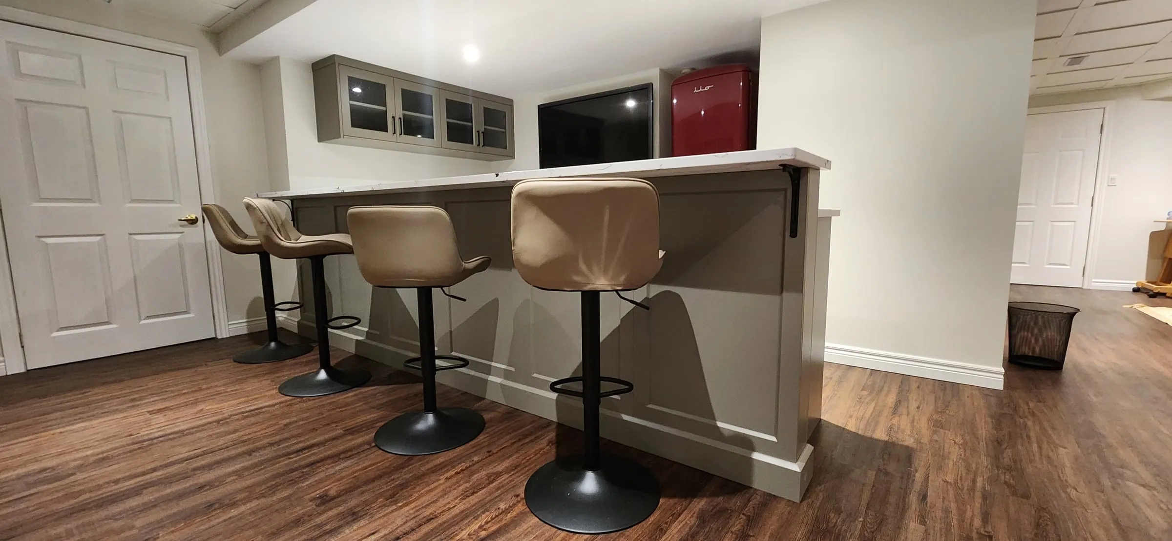 Four tan bar stools along the counter, with the glass cabinets, a TV and the red fridge behind.