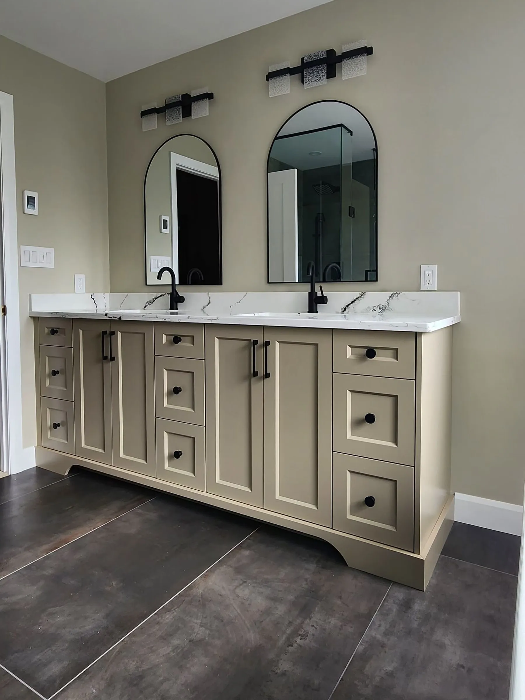 A double vanity with beige shaker cabinets, two black faucets and two arched black mirrors