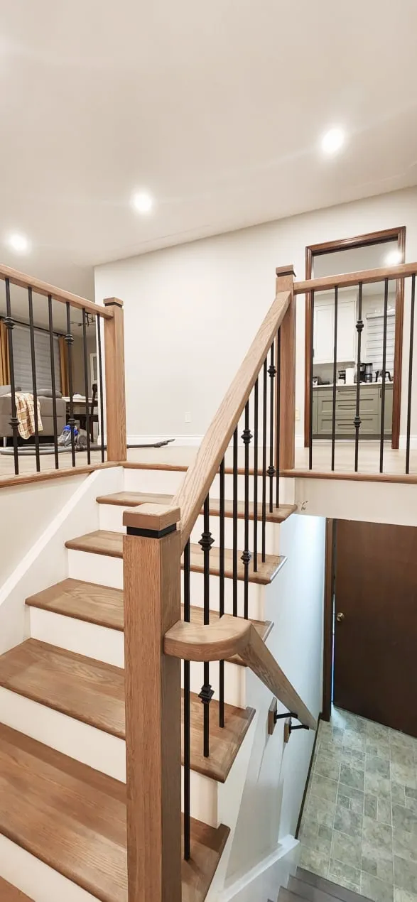 The finished staircase with light wood treads, white risers, wood newel posts and black metal spindles.