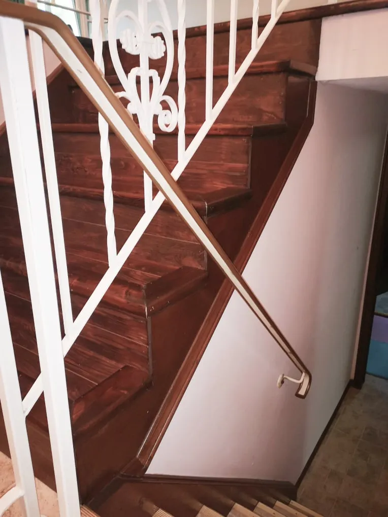 The old staircase from the side before the work, with dark stained treads and white scrolled railings.