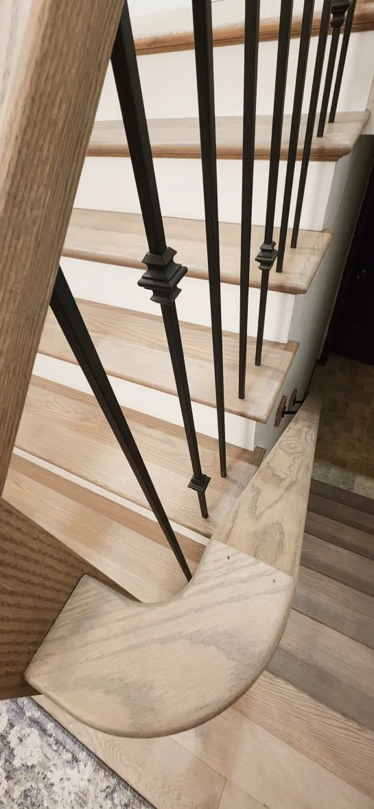 The new railing seen from above, with a curved wood handrail end, black metal spindles and light treads.