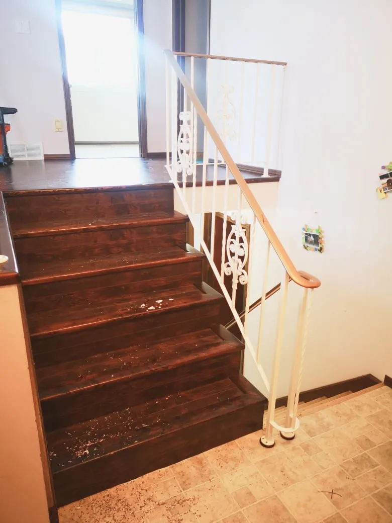 The old stairs before the renovation, with dark brown steps, white scrolled railings and a beige floor below.
