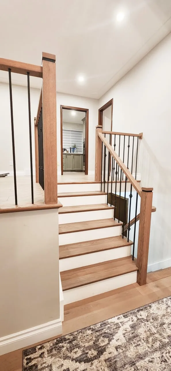 The finished stairs, with light wood treads matching the floor, black spindles and a rug at the bottom.