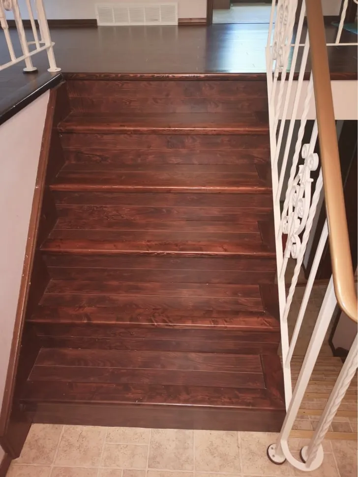 The old stairs before the work, seen from the bottom, with dark reddish-brown steps and a white railing.