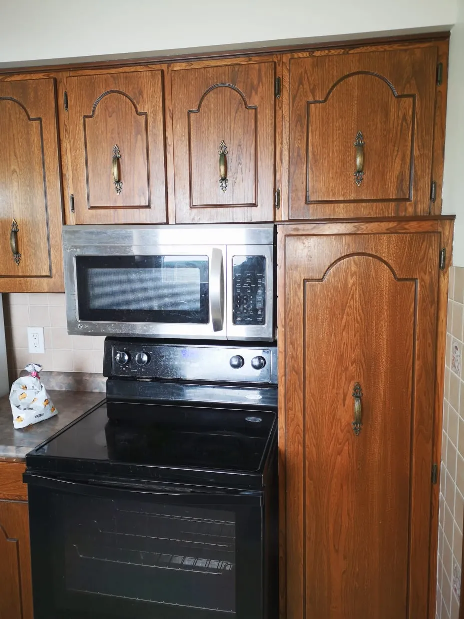 The old kitchen before the renovation, with arched wood cabinet doors around a microwave and black stove.