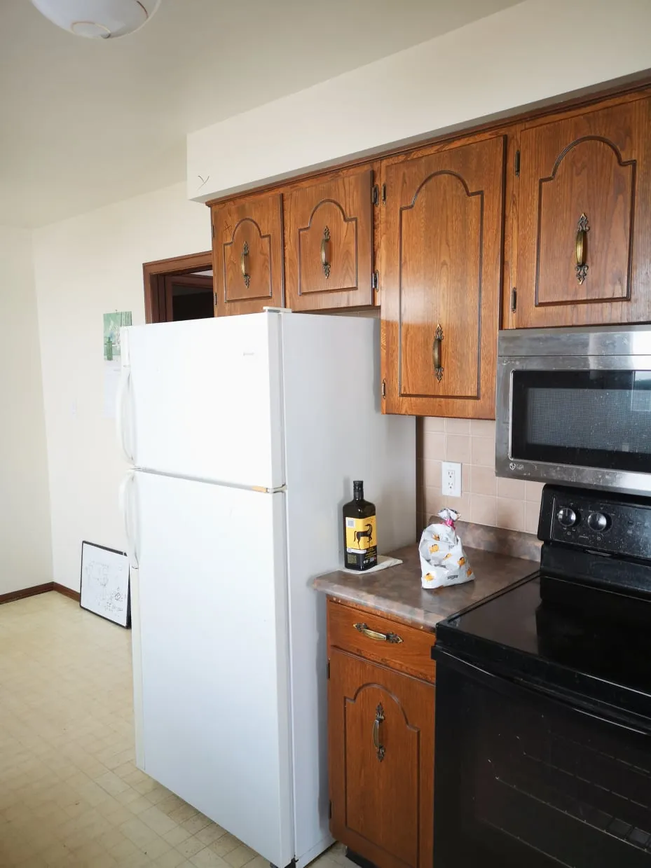 The old kitchen before the renovation, with a white fridge, wood cabinets, a black stove and beige floor.