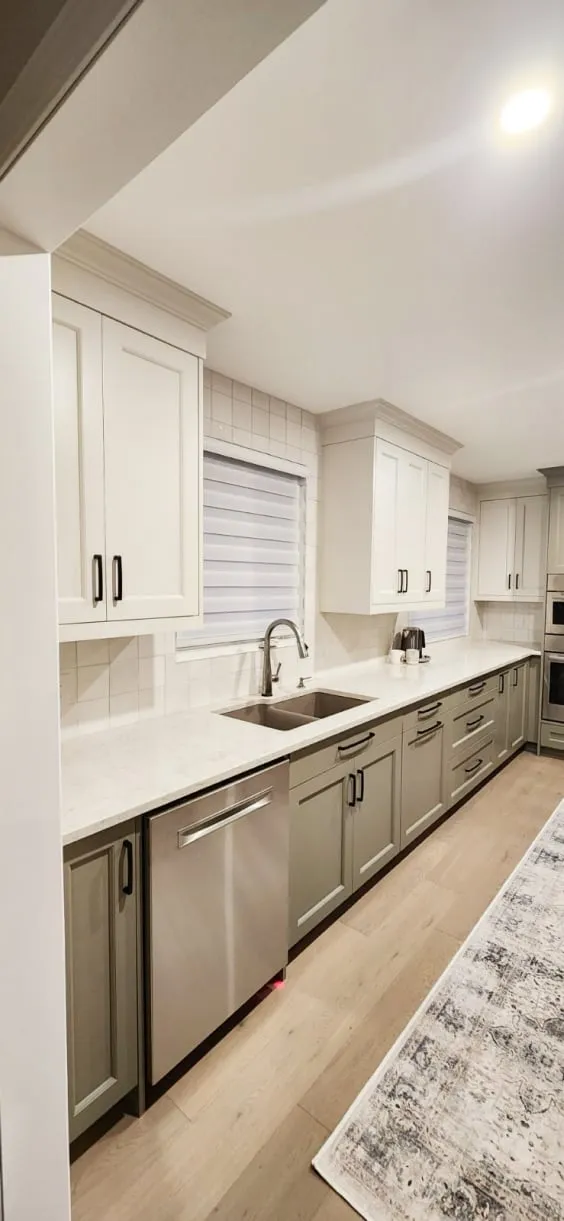 The finished kitchen's long sink counter with white upper cabinets, a white countertop and a runner rug.