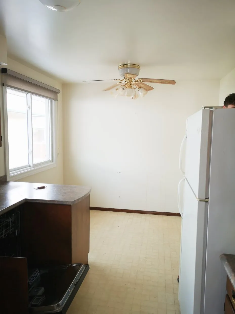 The empty end of the old kitchen before the work, with a beige floor, ceiling fan and window.