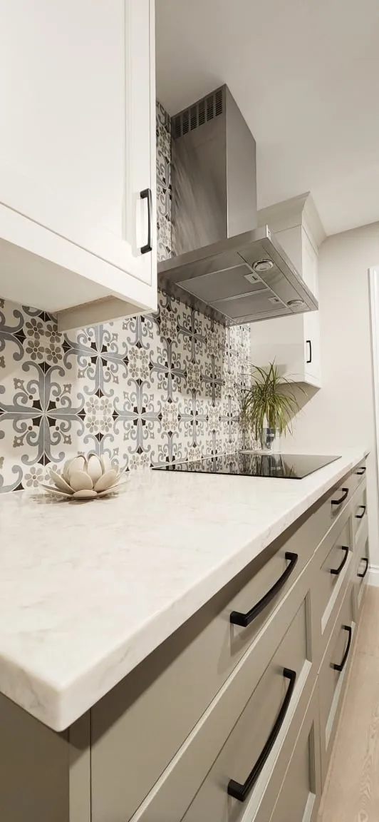 The finished cooktop counter up close, with a blue-grey patterned backsplash, white countertop and black drawer pulls.