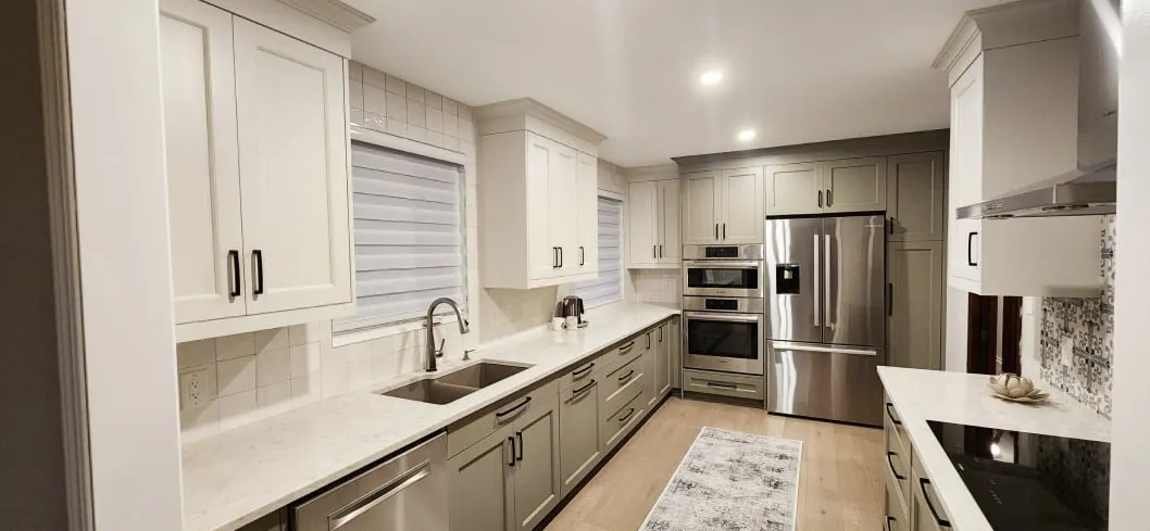 The whole finished kitchen, with sage green and white cabinets, a double sink, a fridge and ceiling lights.
