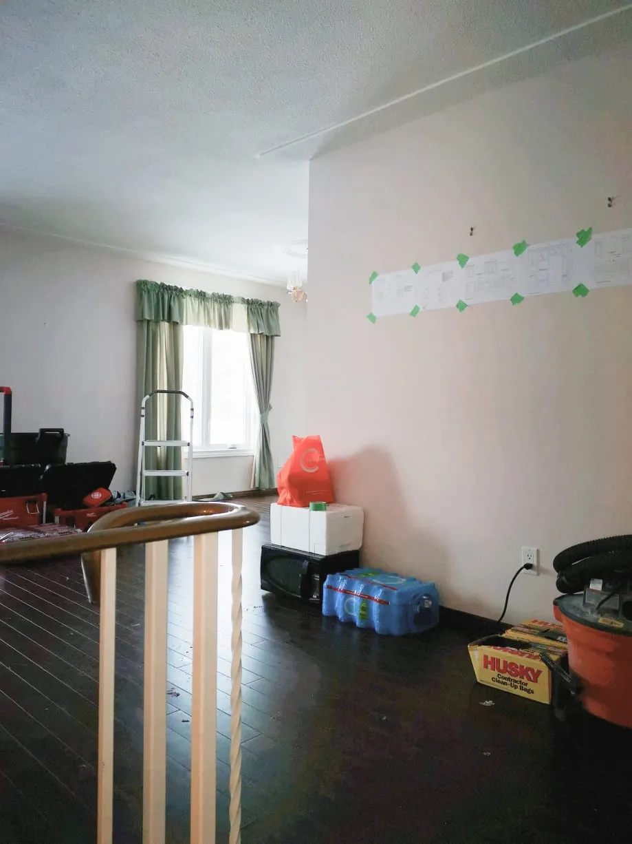 The old living area before the work, with dark floors, green curtains and drawings taped to the wall.