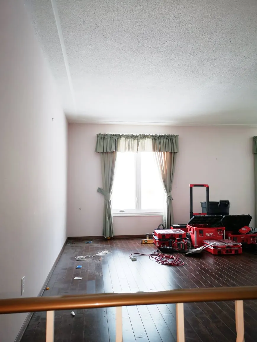 The empty living room before the work, with dark floors, a curtained window and red tool cases.
